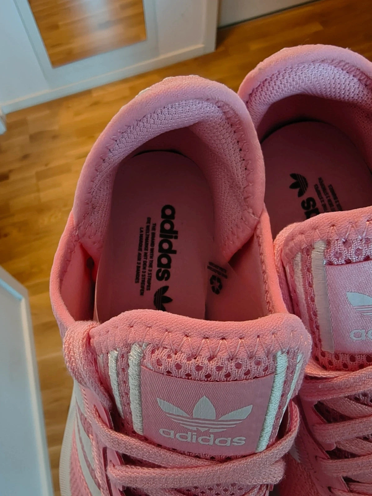 Adidas pink and white trainers with synthetic and textile materials, featuring slip-on and lace-up design.