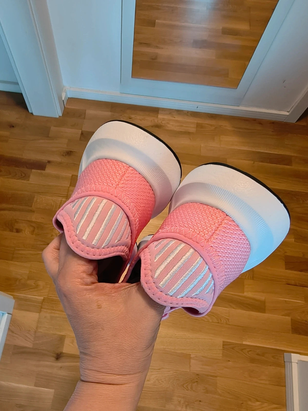 Adidas pink trainers with white stripes, breathable textile upper, and lace-up closure.