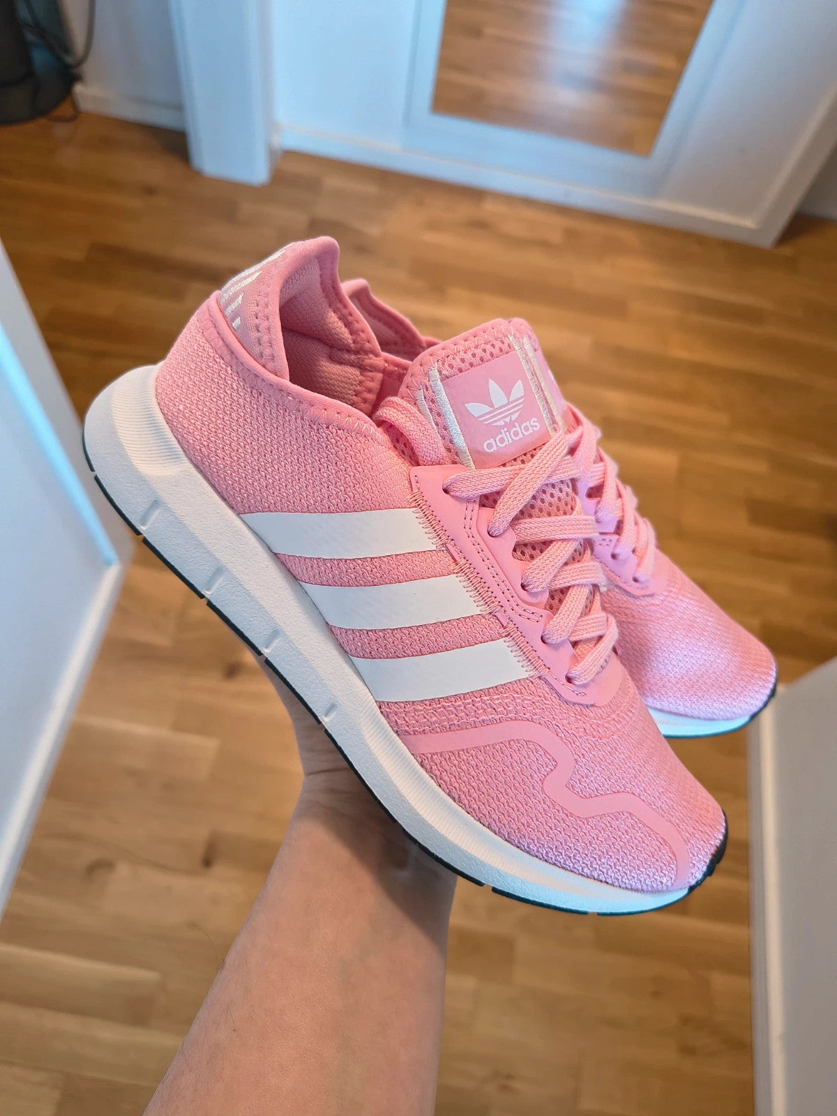 Adidas pink trainers with white stripes, breathable textile upper, and lace-up closure.