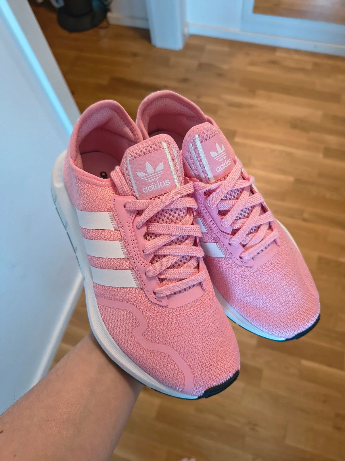 Adidas pink trainers with white stripes, breathable textile upper, and lace-up closure.