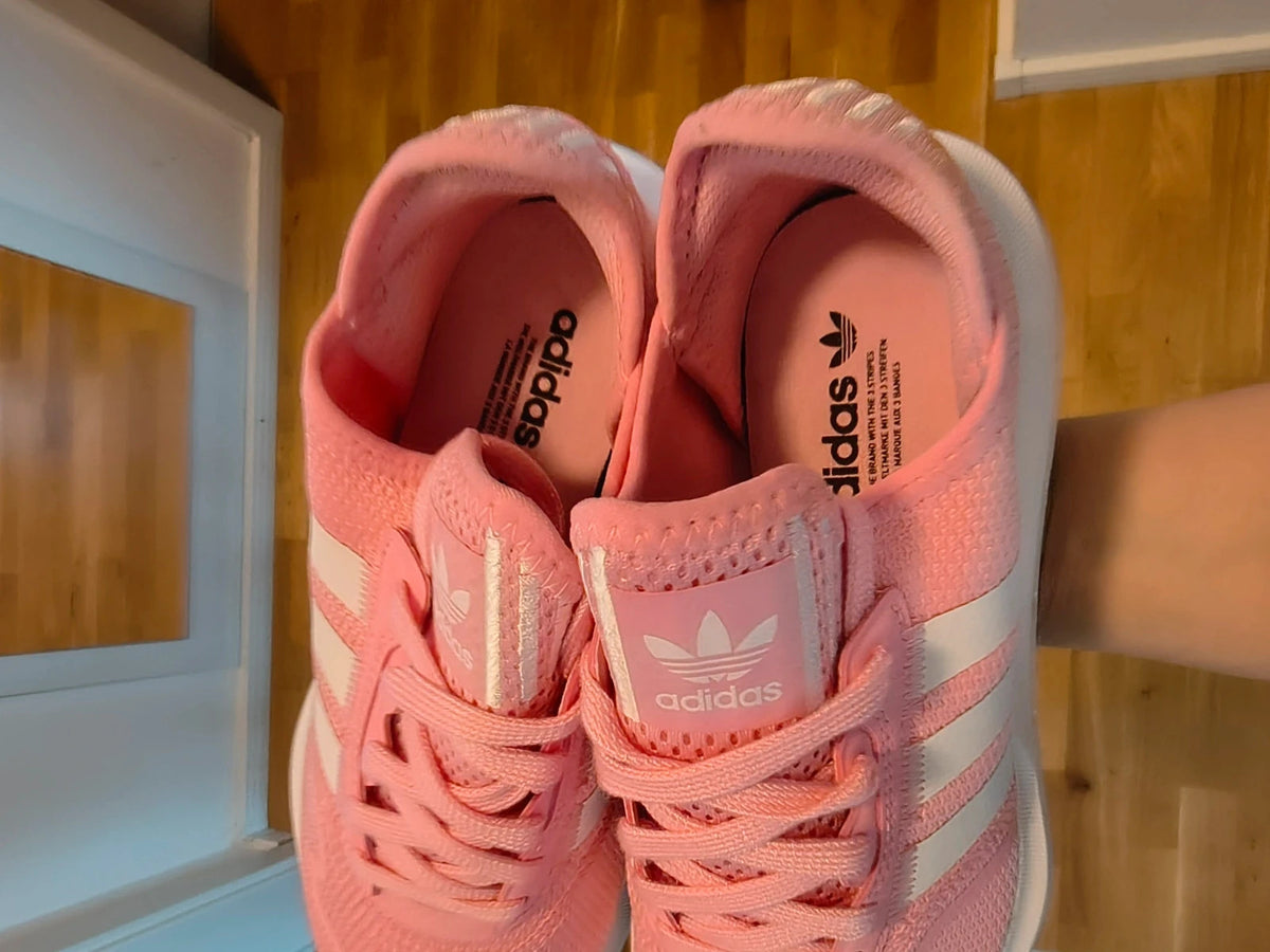 Adidas pink trainers with white stripes, breathable textile upper, and lace-up closure.