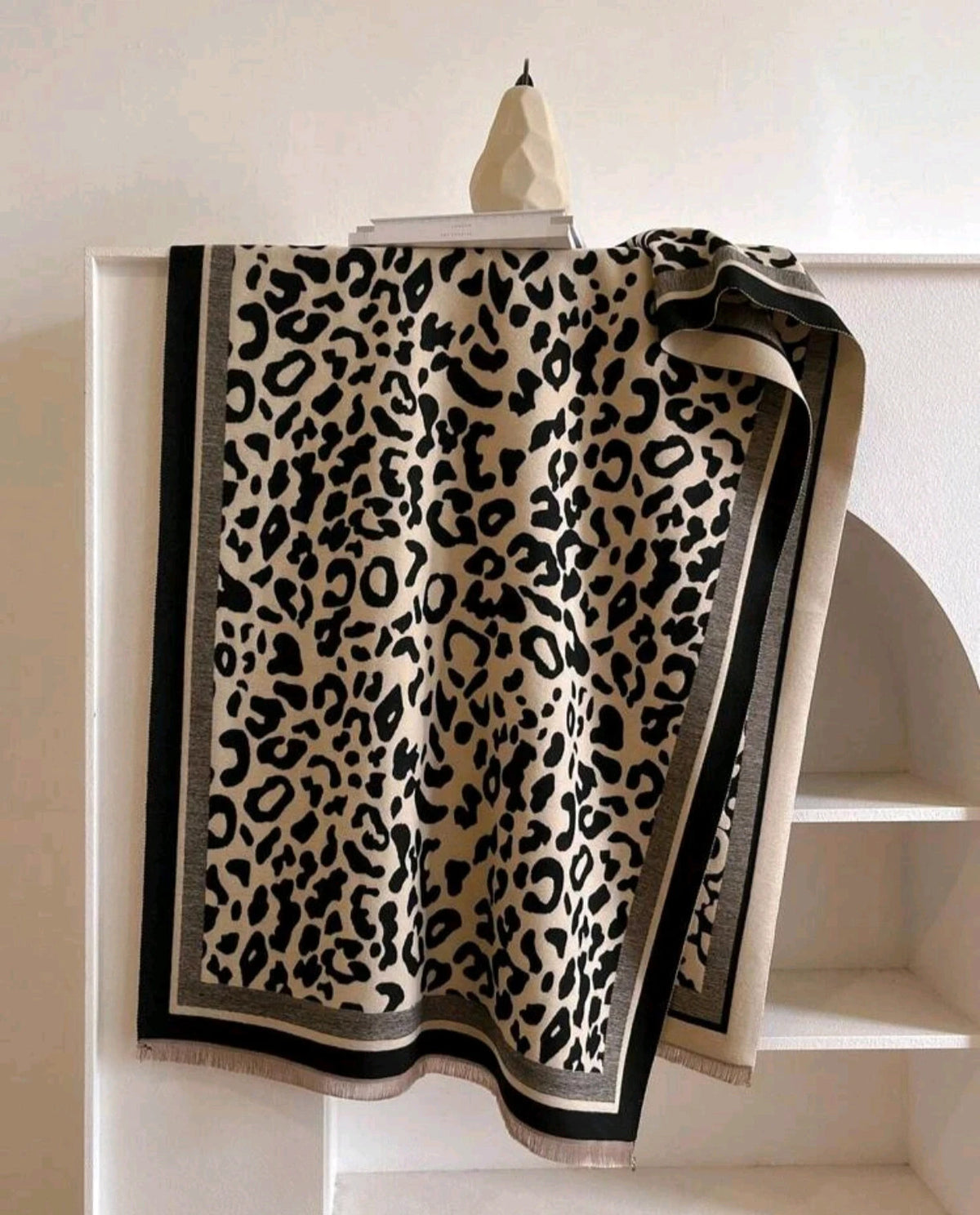 Beige scarf with black leopard print, fringed edges, reversible design, soft polyester material.
