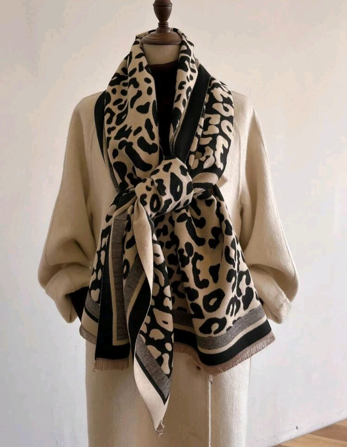 Beige scarf with black leopard print, fringed edges, reversible design, soft polyester material.