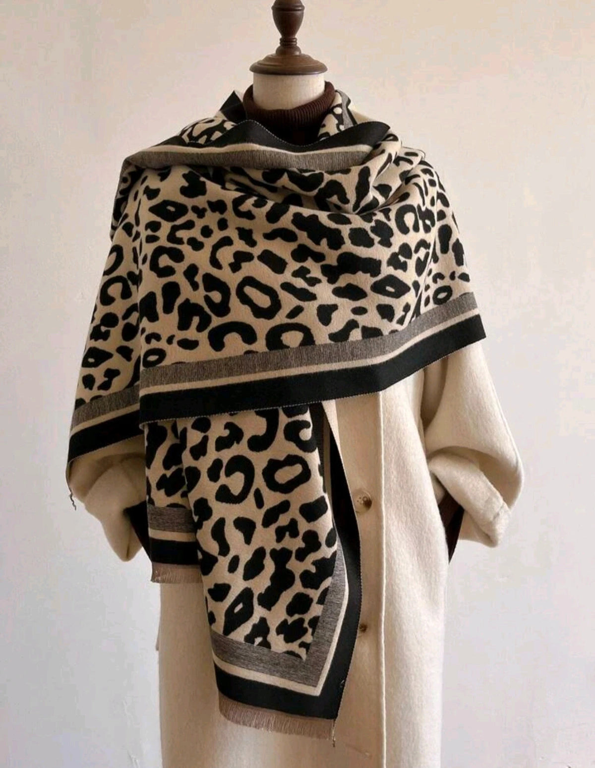 Beige scarf with black leopard print, fringed edges, reversible design, soft polyester material.