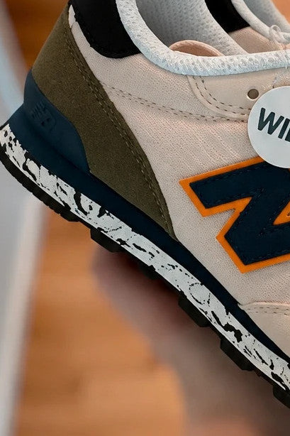 New Balance beige trainers with dark accents, textile and synthetic materials.
