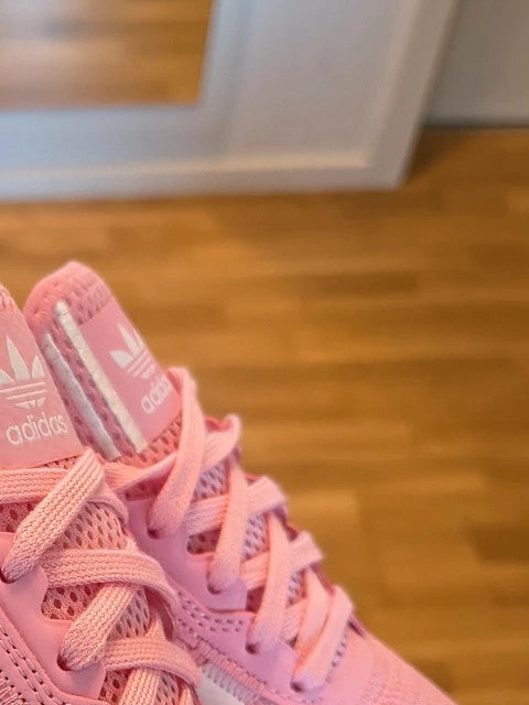 Adidas pink and white trainers with synthetic and textile materials, featuring slip-on and lace-up design.