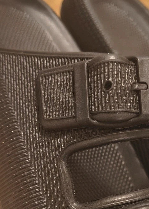 Schwarze Slipper mit zwei verstellbaren Schnallen, leichtes Synthetikmaterial, strukturierte Innensohle.