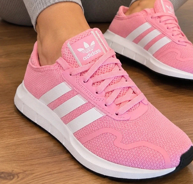 Adidas pink trainers with white stripes, breathable textile upper, and lace-up closure.