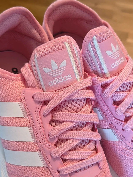 Adidas pink trainers with white stripes, breathable textile upper, and lace-up closure.