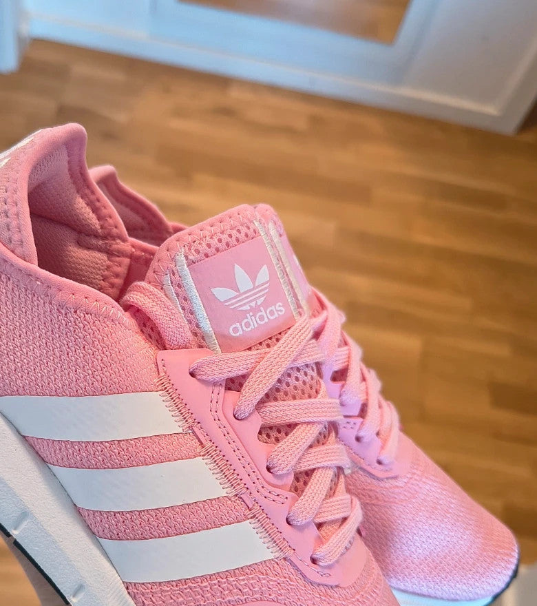 Adidas pink trainers with white stripes, breathable textile upper, and lace-up closure.