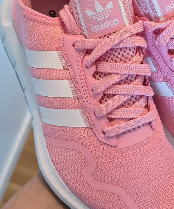 Adidas pink trainers with white stripes, breathable textile upper, and lace-up closure.