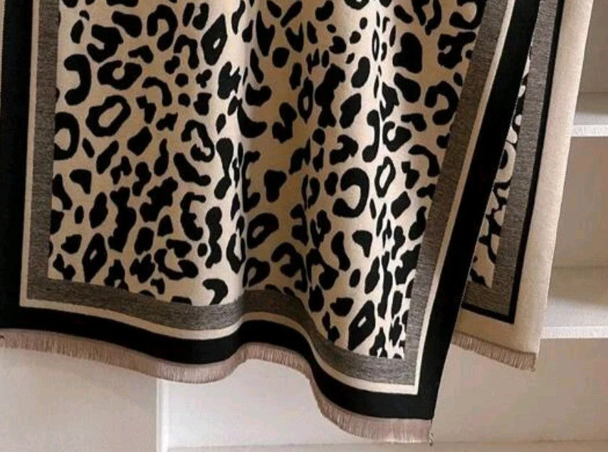 Beige scarf with black leopard print, fringed edges, reversible design, soft polyester material.